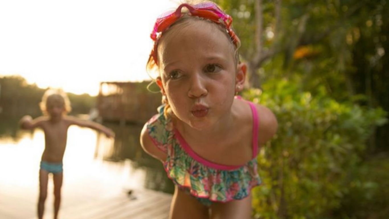 Menina loira e menino brincando na doca da lagoa em trajes de banho